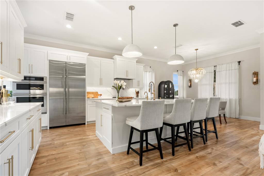A bright kitchen features white cabinetry, a large marble-topped island with bar seating, and stainless-steel appliances — 2549 PALM AVENUE, FLAGLER BEACH, FL