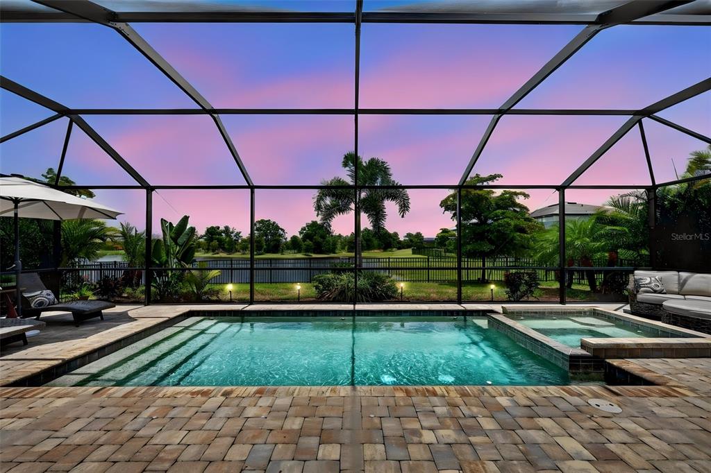 A screened-in patio features a swimming pool and spa overlooking a lake at sunset — 4881 SEAFOAM TRAIL, BRADENTON, FL