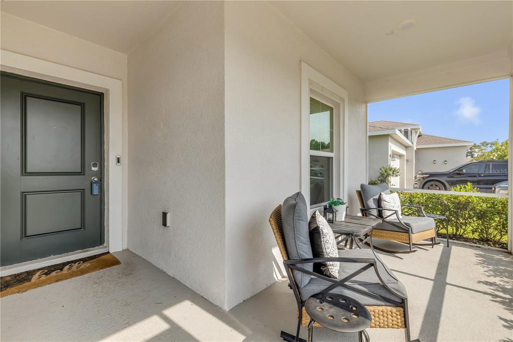 A covered front porch features a dark door, two wicker chairs, and a small table — 3986 WILLOWBROOK DRIVE, EDGEWATER, FL