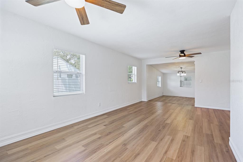 A bright, empty living room with white walls, wood-look flooring, and two ceiling fans — 4006 S SHAMROCK ROAD, TAMPA, FL