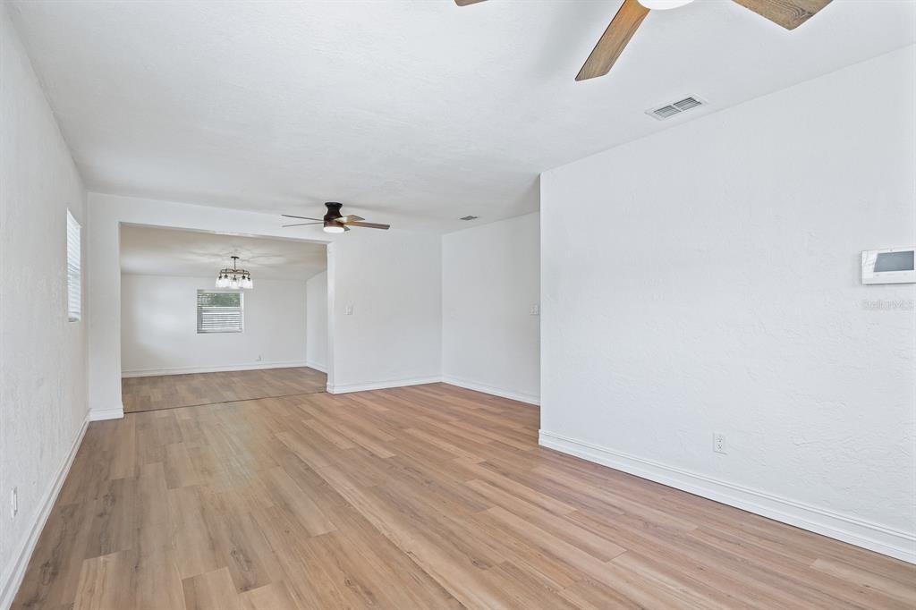An open-concept living area features light wood-look flooring, white walls, and two ceiling fans — 4006 S SHAMROCK ROAD, TAMPA, FL