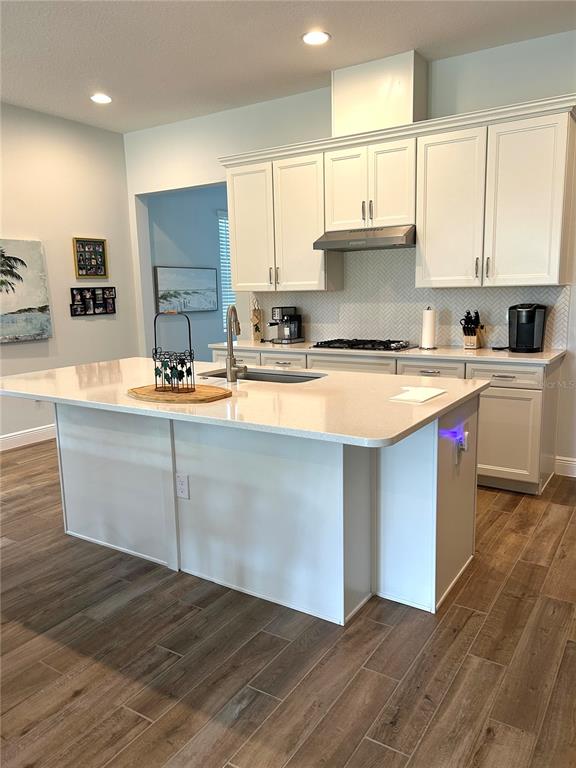 A modern kitchen features white cabinetry, a large quartz island, and wood-look tile flooring — 2042 KEY BAY TRAIL, KISSIMMEE, FL
