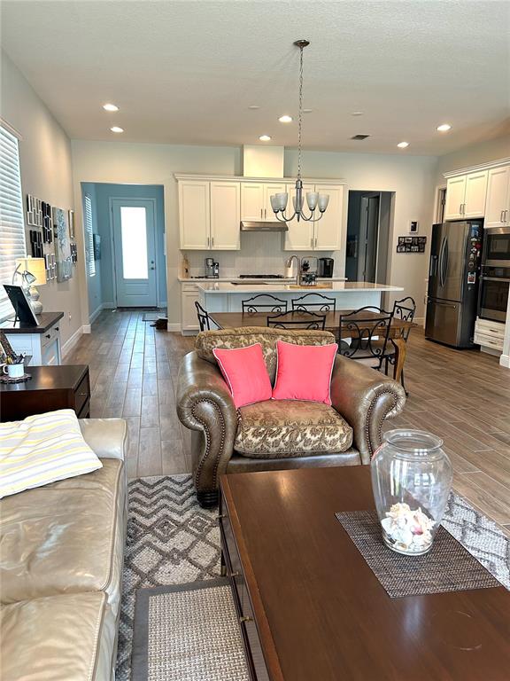 An open-concept kitchen and living area features white cabinetry, wood-look tile flooring, and a dining table — 2042 KEY BAY TRAIL, KISSIMMEE, FL
