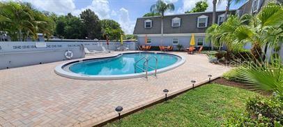 An outdoor swimming pool is surrounded by a brick paver deck and a multi-story building — 1712 BELLEAIR FOREST DRIVE UNIT A, BELLEAIR, FL