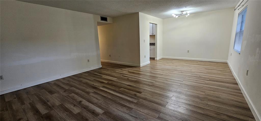 An empty living room features light-colored walls, wood-look laminate flooring, and a ceiling light fixture — 1712 BELLEAIR FOREST DRIVE UNIT A, BELLEAIR, FL
