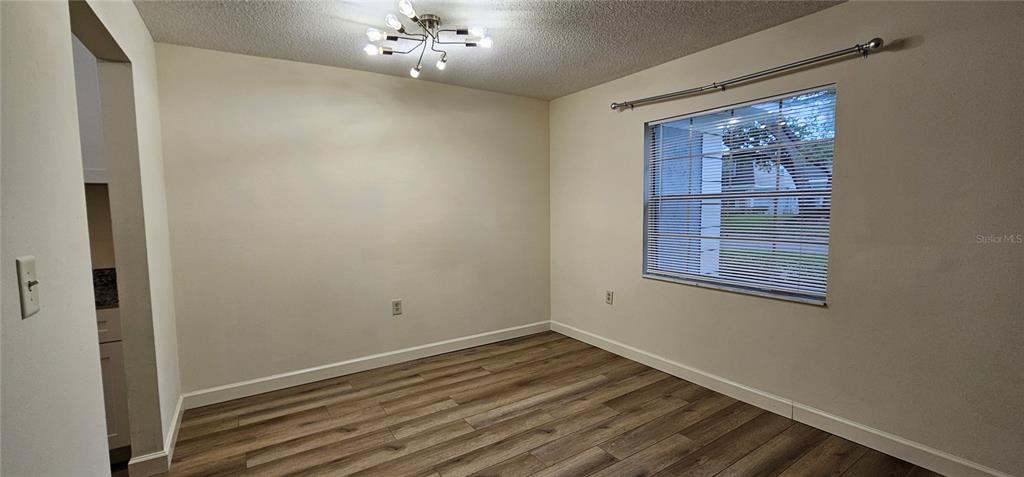 This dining room features light-colored walls, wood-look flooring, a modern light fixture, and a window — 1712 BELLEAIR FOREST DRIVE UNIT A, BELLEAIR, FL