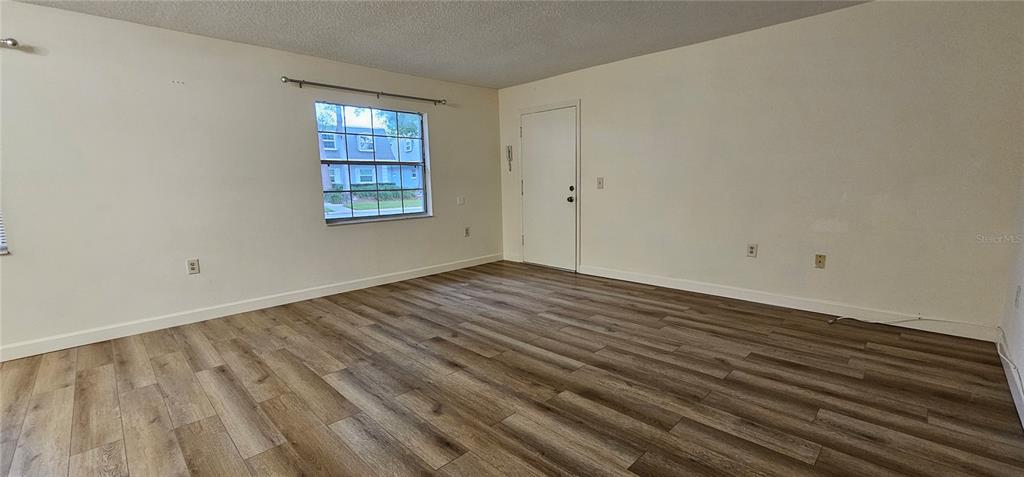 An empty room features light-colored walls, wood-look laminate flooring, and a single window — 1712 BELLEAIR FOREST DRIVE UNIT A, BELLEAIR, FL