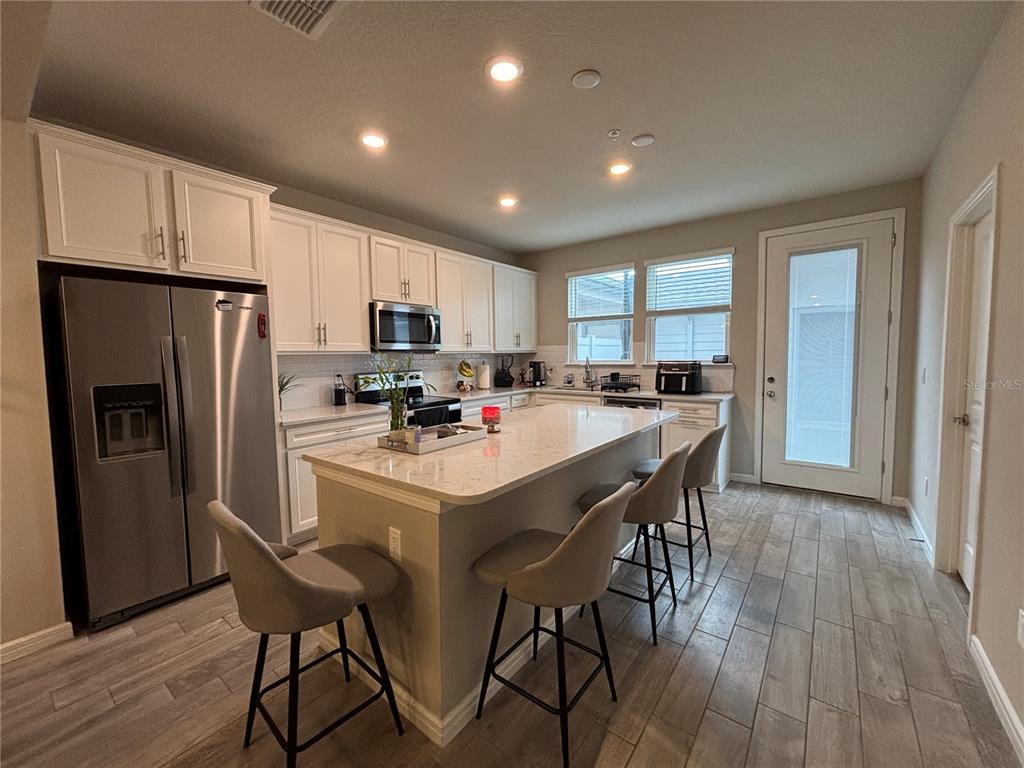 A modern kitchen features white cabinets, stainless steel appliances, a quartz island, and wood-look tile flooring — 14550 ORCHID ISLAND DRIVE, ORLANDO, FL