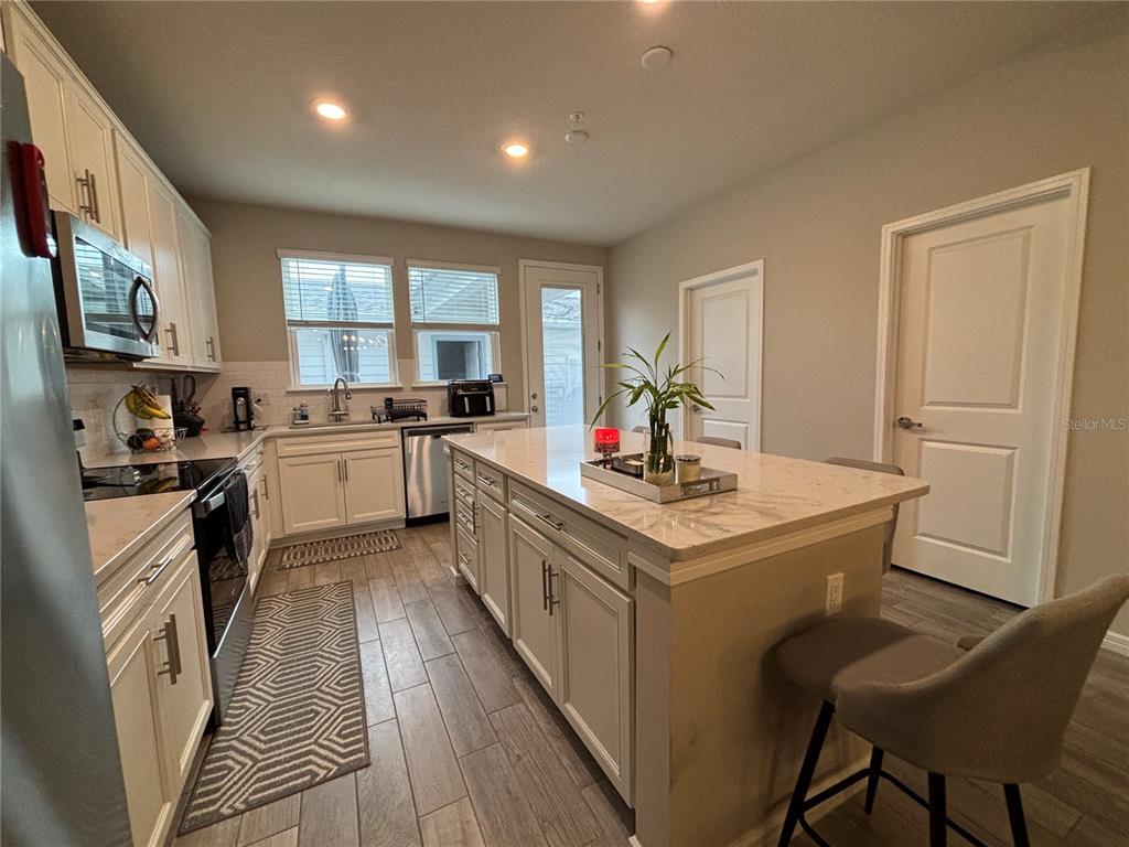A kitchen features white cabinetry, a large center island with seating, and wood-look tile flooring — 14550 ORCHID ISLAND DRIVE, ORLANDO, FL