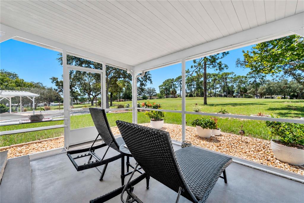 A screened-in porch features two lounge chairs overlooking a grassy yard and trees — 8241 WEATHERFORD AVENUE, BROOKSVILLE, FL
