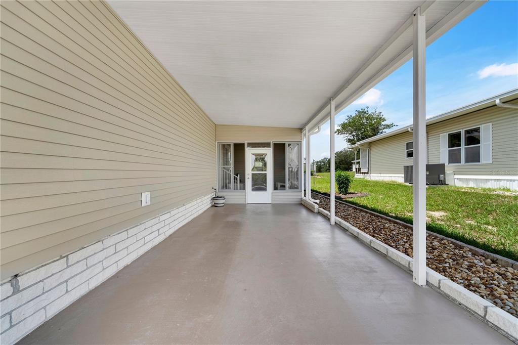 A covered concrete patio with light-colored siding and a white door leads to the entrance — 8241 WEATHERFORD AVENUE, BROOKSVILLE, FL