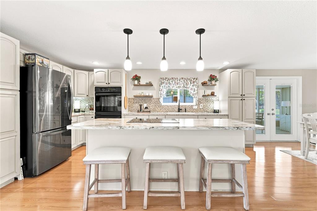 A kitchen features a central island with three stools, light cabinetry, and stainless steel appliances — 8241 WEATHERFORD AVENUE, BROOKSVILLE, FL