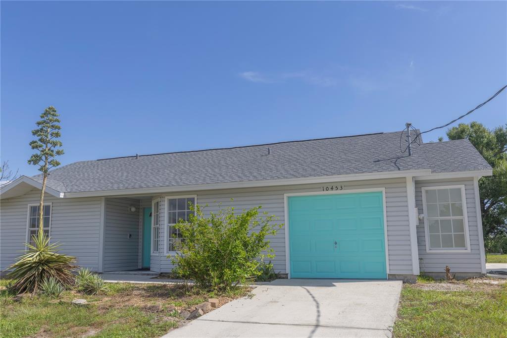 A single-story house with light gray siding, a bright turquoise garage door, and a front yard — 10453 GREENWAY AVENUE, ENGLEWOOD, FL