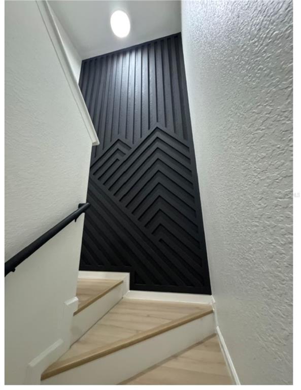 A staircase with light wood steps and a black geometric mountain-themed accent wall — 16320 PARKSTONE PALMS COURT, TAMPA, FL
