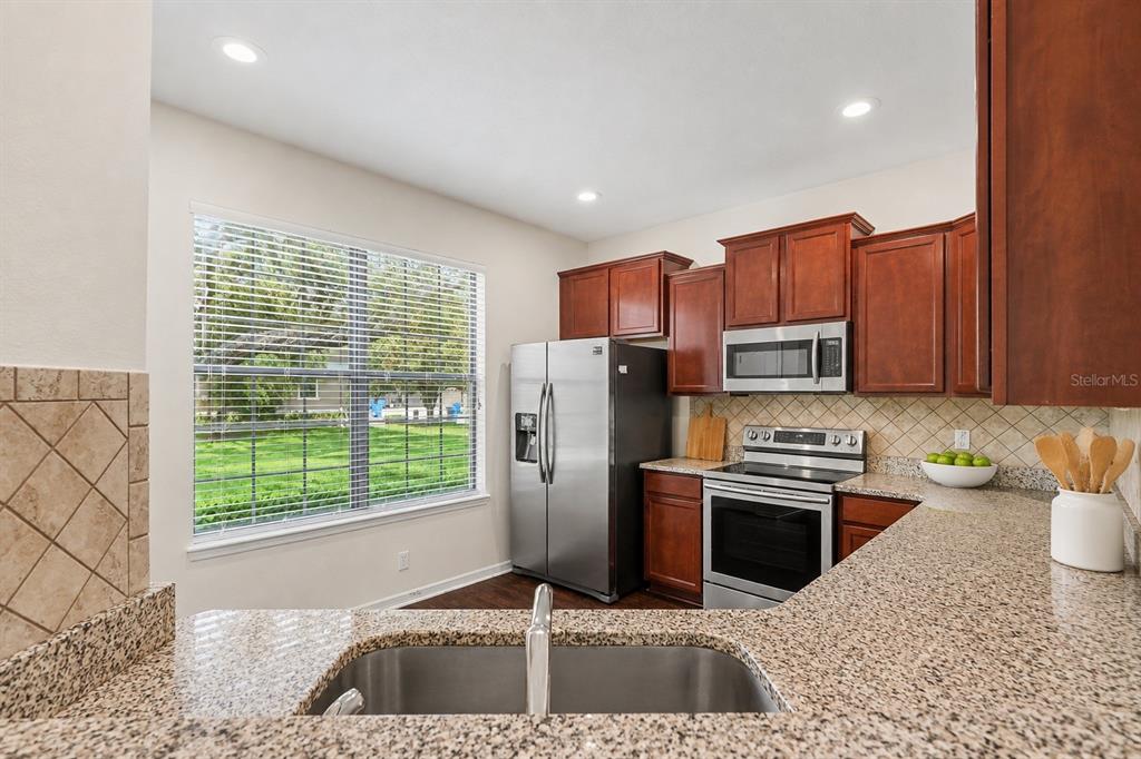 A kitchen with dark wood cabinets, stainless steel appliances, granite countertops, and a large window — 5520 KINGLETHILL DRIVE, LITHIA, FL
