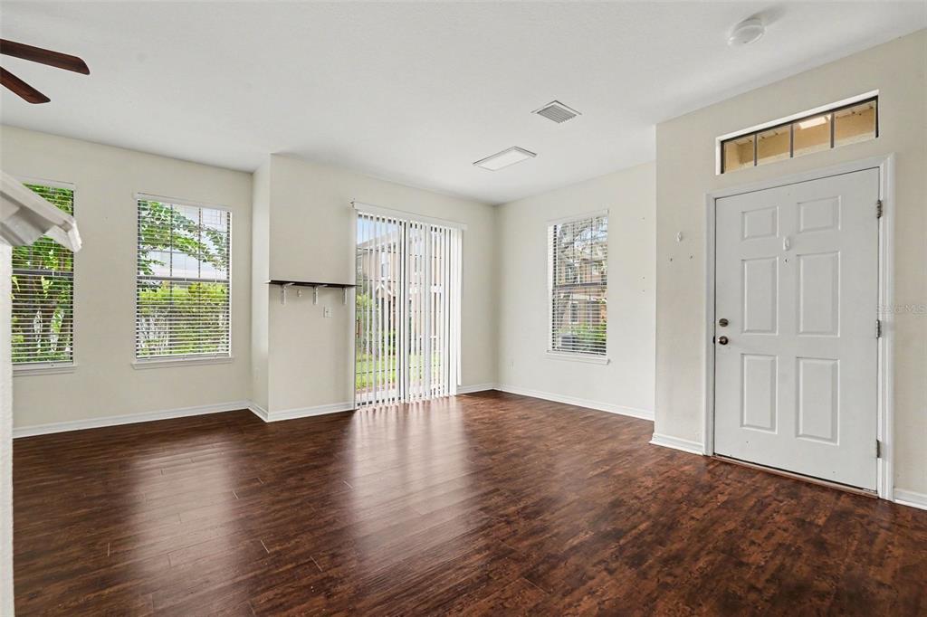 An empty living room features dark wood-look flooring, white walls, a sliding glass door, and windows — 5520 KINGLETHILL DRIVE, LITHIA, FL