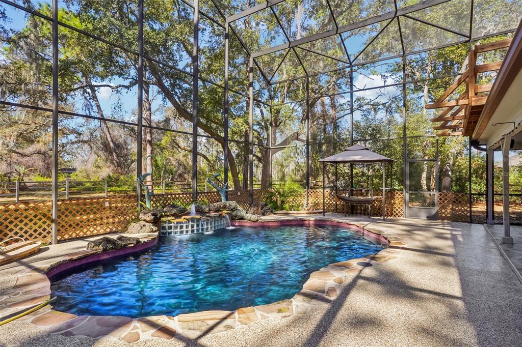 A screened-in pool area features a rock waterfall, stone decking, and a small gazebo — 29207 OLD MILL W, TAVARES, FL