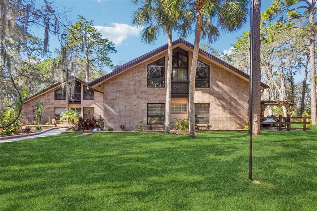 A two-story brick house with a gabled roof sits behind a large green lawn — 29207 OLD MILL W, TAVARES, FL