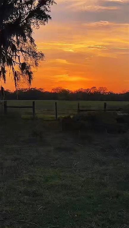 A vibrant orange sunset illuminates a grassy field with a wooden fence and silhouetted trees — 3650 NE 95TH STREET, ANTHONY, FL
