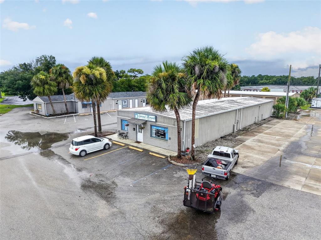 An aerial view shows a commercial building with palm trees, a parking lot, and vehicles — 3207 13TH STREET, ST CLOUD, FL