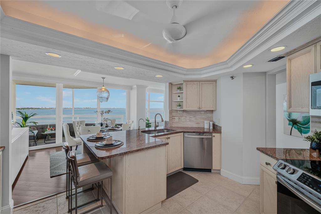 A kitchen with granite countertops and light wood cabinets overlooks a dining area and water — 888 BLVD OF THE ARTS UNIT 1008, SARASOTA, FL