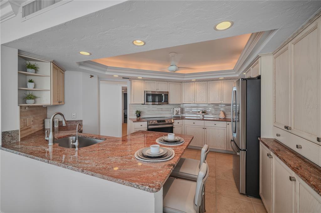 A kitchen features light wood cabinets, granite countertops, a breakfast bar, and stainless steel appliances — 888 BLVD OF THE ARTS UNIT 1008, SARASOTA, FL