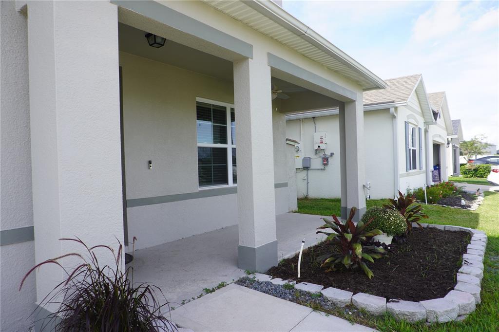 A covered concrete porch features two lounge chairs, a small table, and a stone planter — 323 HARBOUR WAY, MULBERRY, FL