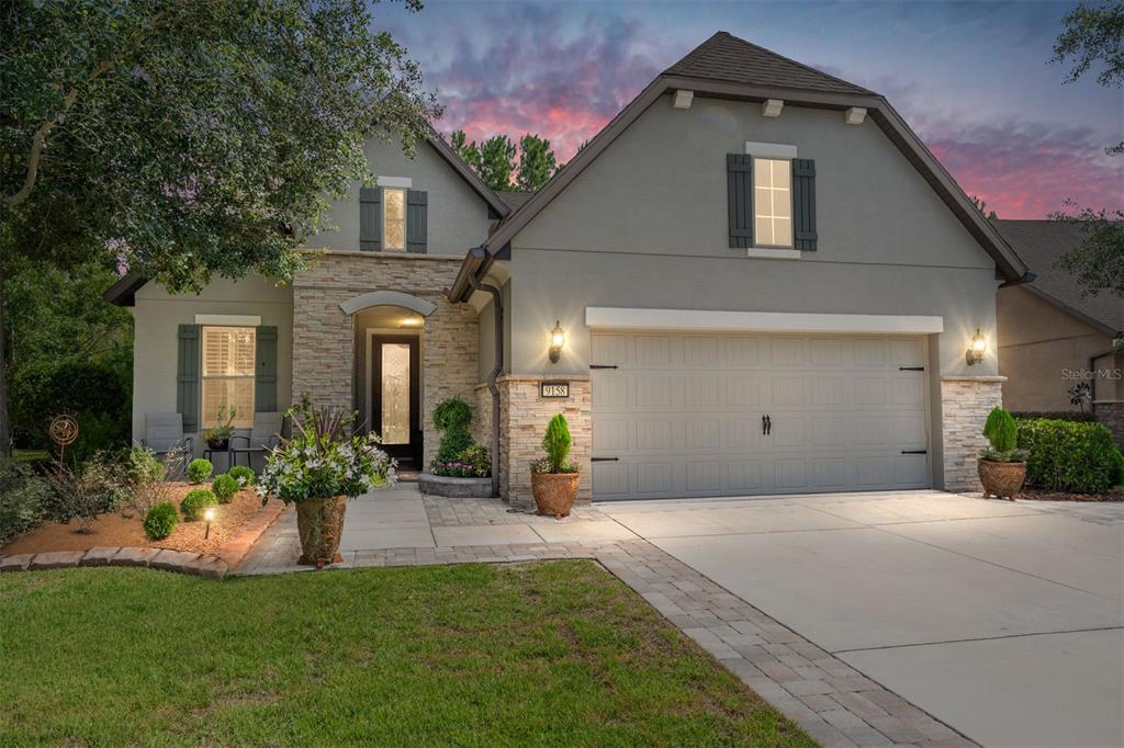 A two-story house with a stone-accented facade, gray stucco, and a two-car garage at dusk — 9158 SW 65TH LOOP, OCALA, FL