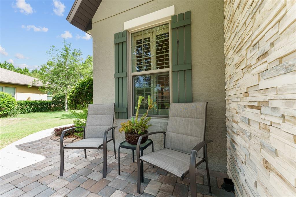 A patio with two chairs and a small table sits outside a stone-accented house wall — 9158 SW 65TH LOOP, OCALA, FL