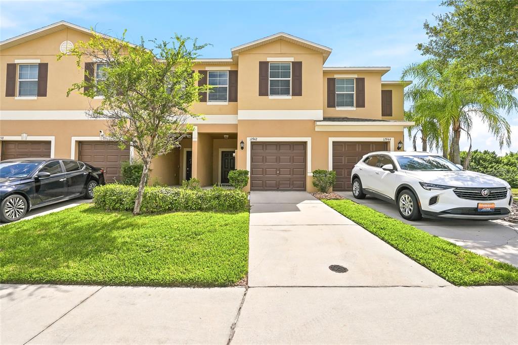 A two-story tan townhouse with two garages and two parked cars in the driveway — 12942 UTOPIA GARDENS WAY, RIVERVIEW, FL