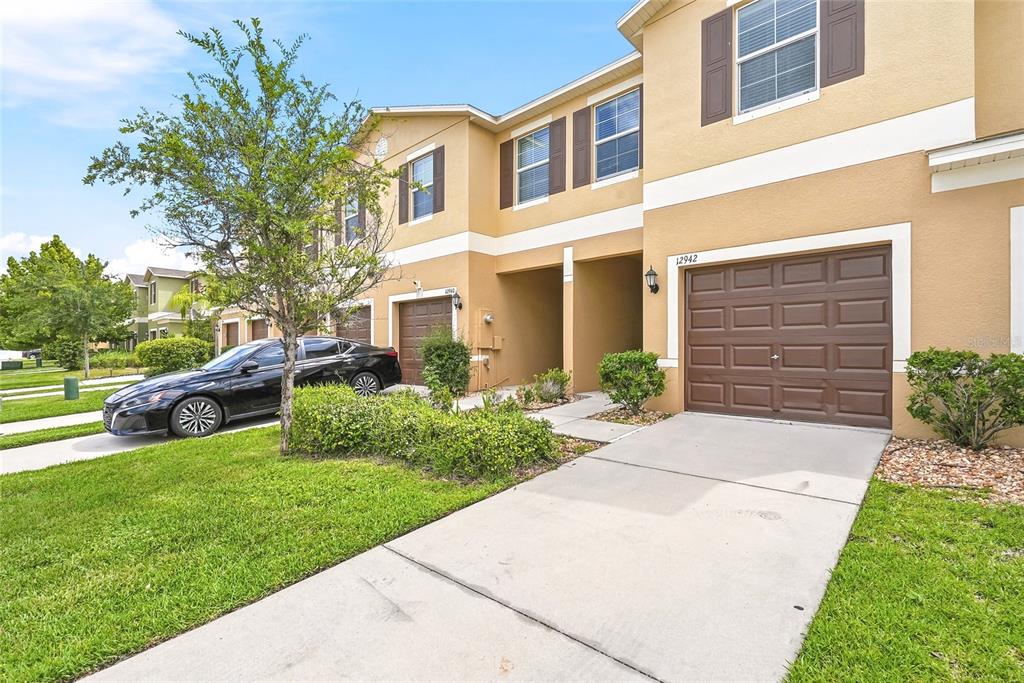 A two-story townhouse exterior features a brown garage door, tan stucco walls, and a driveway — 12942 UTOPIA GARDENS WAY, RIVERVIEW, FL