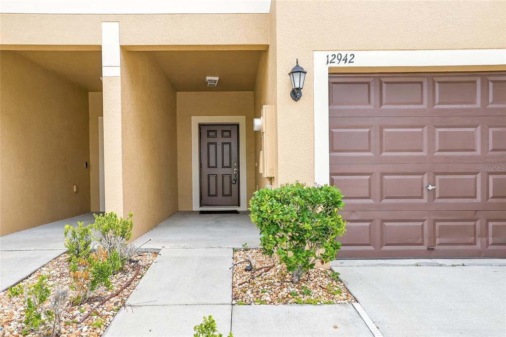 The exterior view shows a tan house with a brown garage door and front door — 12942 UTOPIA GARDENS WAY, RIVERVIEW, FL