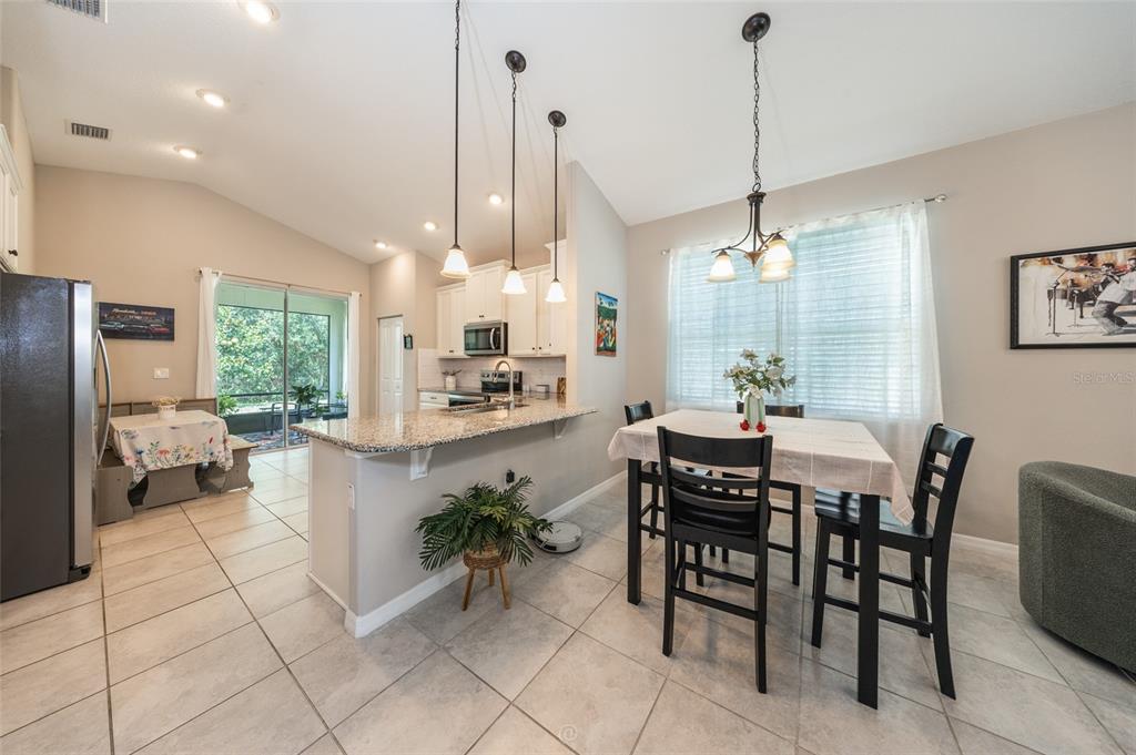 A kitchen with granite countertops and a dining area with a table and chairs — 153 PARK PLACE CIRCLE, PALM COAST, FL