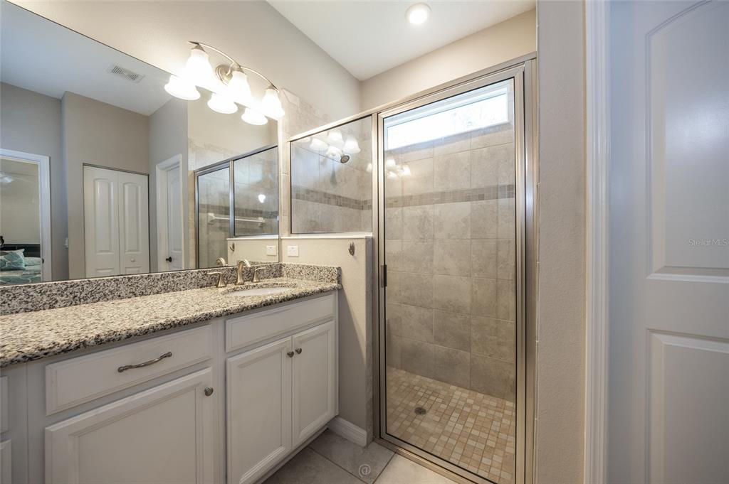 A bathroom features a granite vanity, white cabinets, and a tiled walk-in shower with glass — 153 PARK PLACE CIRCLE, PALM COAST, FL