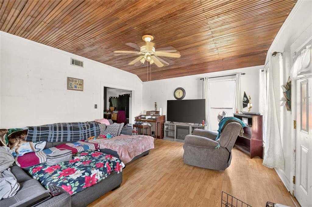 A living room features a wood-paneled vaulted ceiling, light wood flooring, and a dark sectional sofa — 7020 SE 221ST STREET, HAWTHORNE, FL