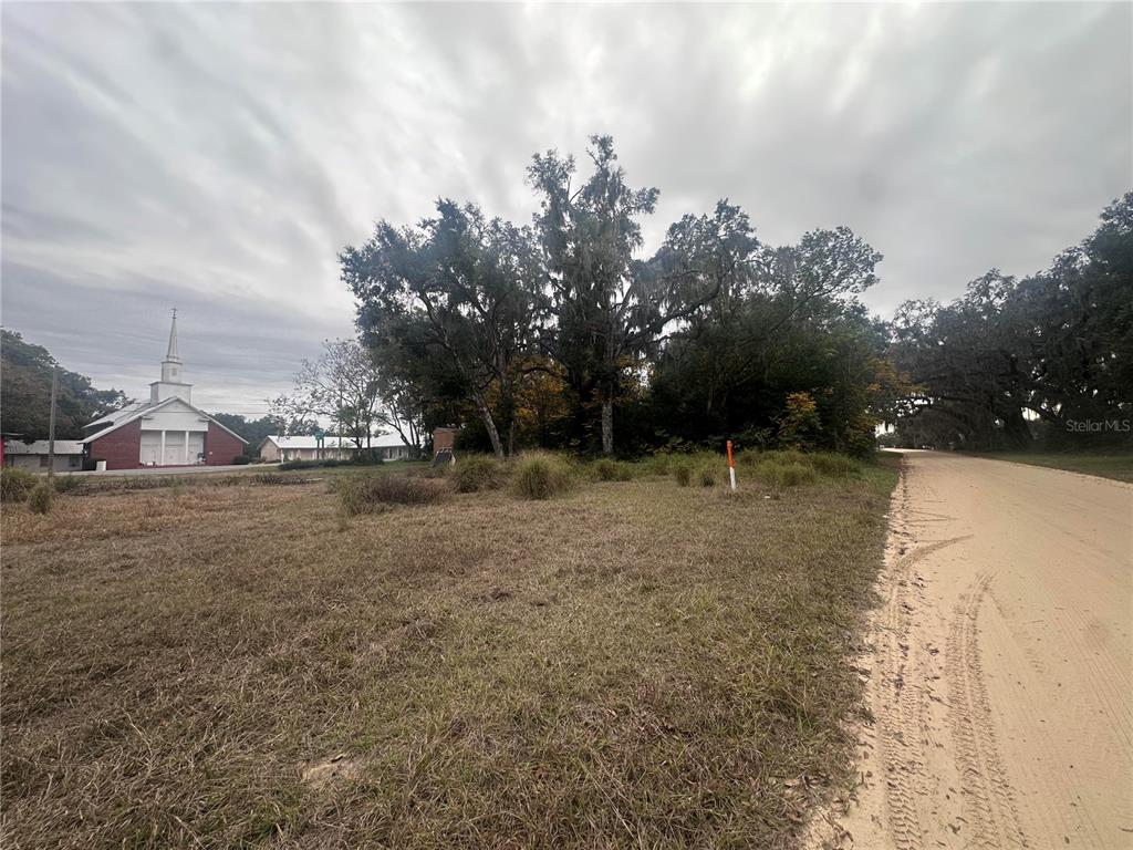 A vacant, grassy lot sits beside a dirt road with a church in the background — SR-19, ALTOONA, FL