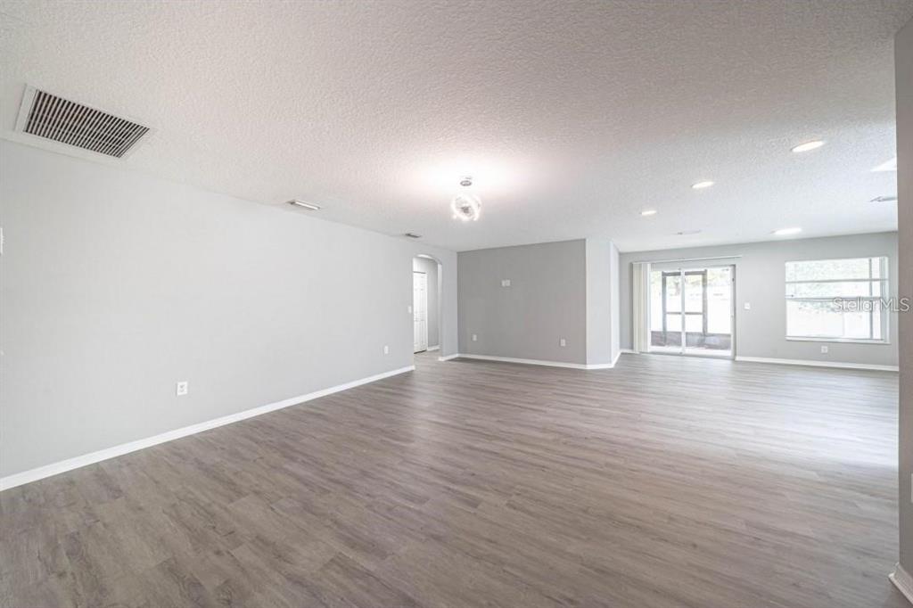 A spacious, open-concept living area features light gray walls and wood-look flooring — 2025 PEACEFUL PALM STREET, RUSKIN, FL