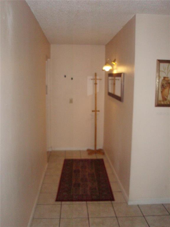 A hallway with beige walls, tile flooring, a runner rug, and a wooden coat rack — 4500 E BAY DRIVE UNIT 138, CLEARWATER, FL