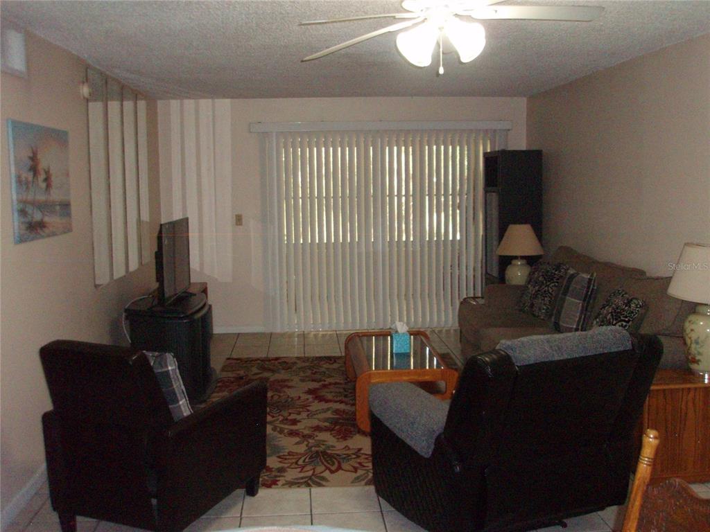 A living room features tile flooring, a ceiling fan, vertical blinds, and assorted furniture — 4500 E BAY DRIVE UNIT 138, CLEARWATER, FL