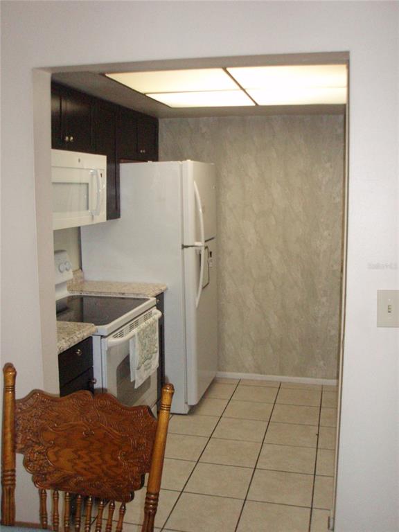 A kitchen with dark cabinets, white appliances, granite countertops, and light-colored tile flooring — 4500 E BAY DRIVE UNIT 138, CLEARWATER, FL