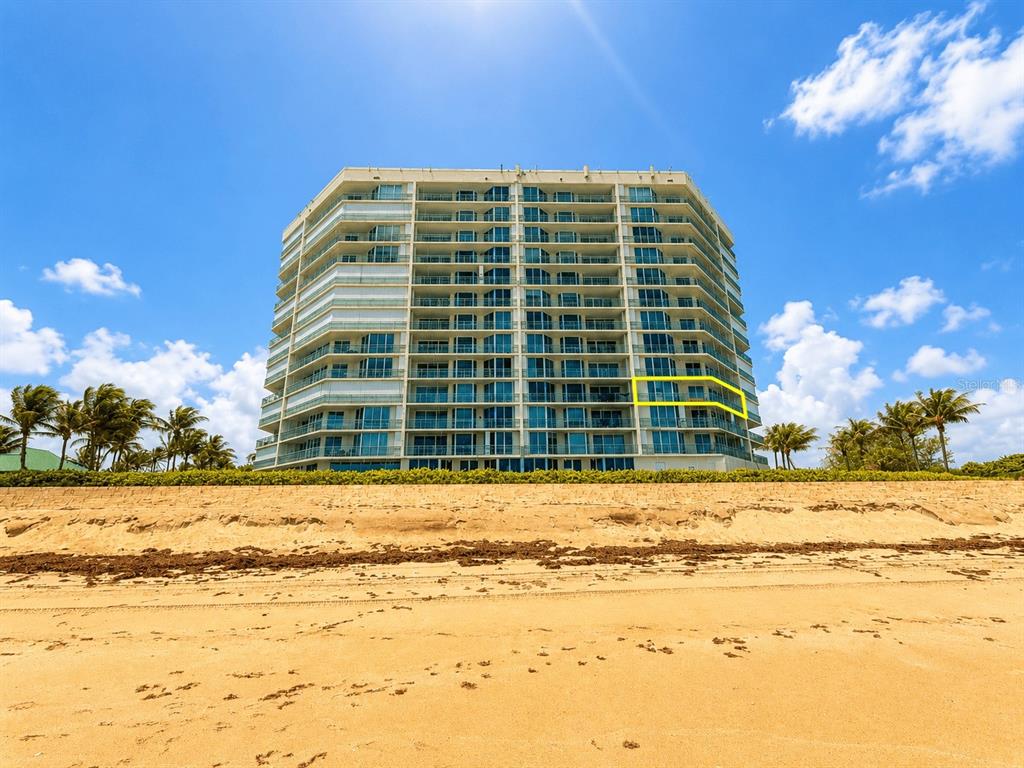 A multi-story beachfront condominium building stands behind a sandy beach under a blue sky — 8600 S OCEAN DRIVE UNIT 402, JENSEN BEACH, FL