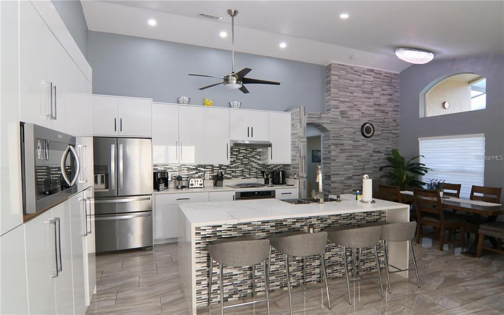 A modern kitchen features white cabinets, a marble-topped island with bar stools, and stone accents — 1470 WEDGE WAY, HAINES CITY, FL