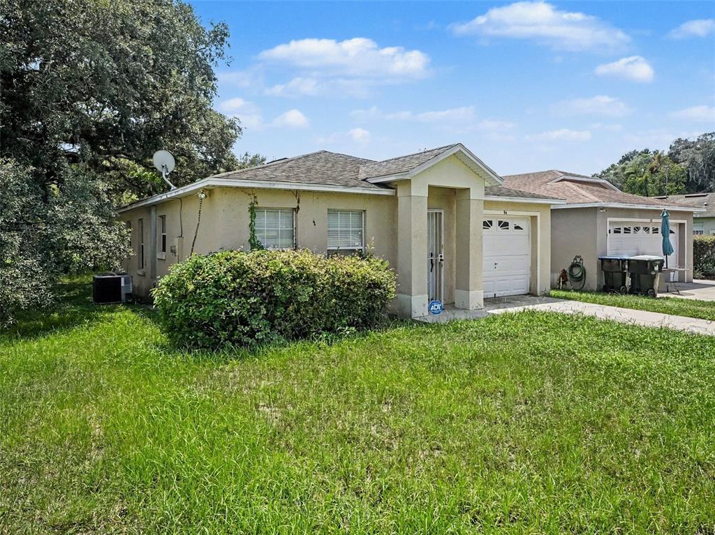 A single-story house with a beige stucco exterior, a small front lawn, and a garage — 94 E 18TH STREET, APOPKA, FL
