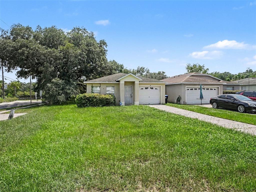 A single-story suburban house with a tan exterior, a garage, and a large front lawn — 94 E 18TH STREET, APOPKA, FL