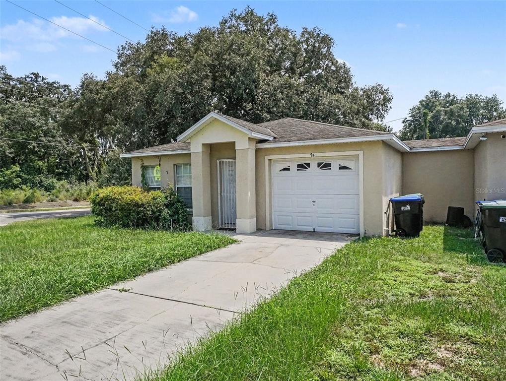A single-story house with a white garage door, a concrete driveway, and a small front yard — 94 E 18TH STREET, APOPKA, FL
