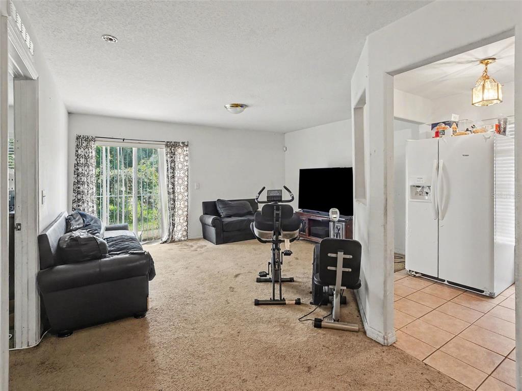 A living room with carpeted floors, a black sofa, exercise equipment, and an adjacent kitchen — 94 E 18TH STREET, APOPKA, FL