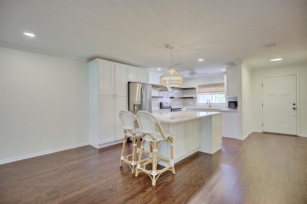A kitchen features white cabinetry, a central island with two stools, and dark wood flooring — 3855 RODEO DRIVE, SEBRING, FL
