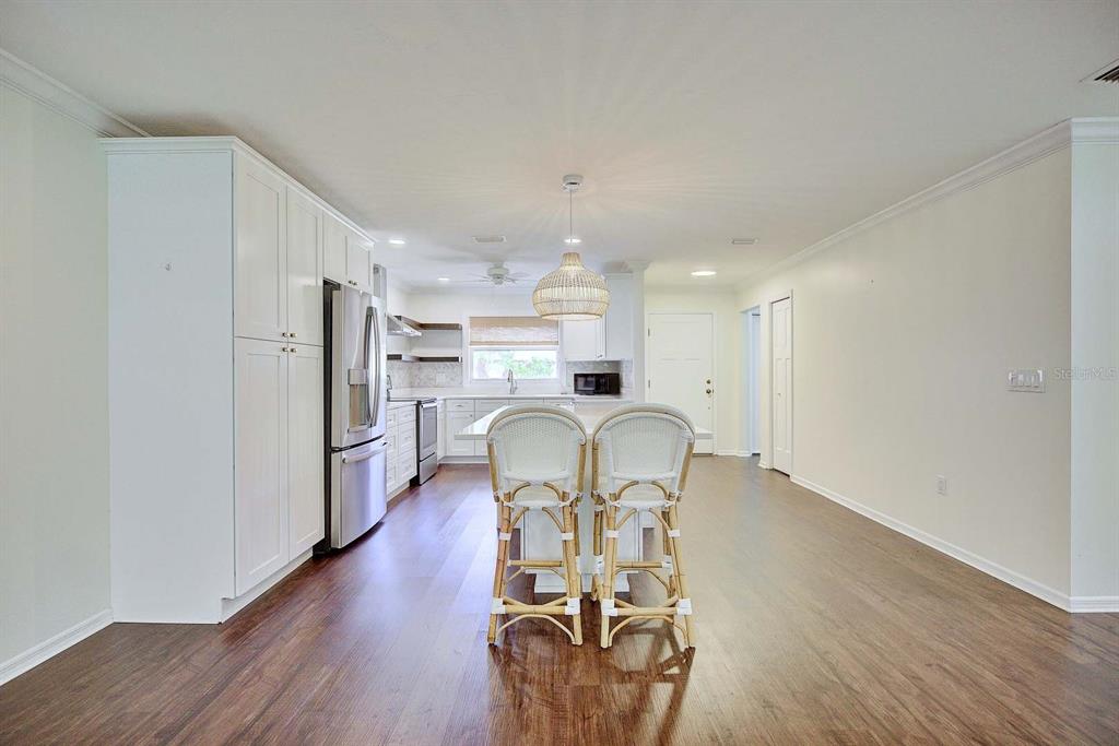 A kitchen features white cabinets, a central island with two stools, and wood-look flooring — 3855 RODEO DRIVE, SEBRING, FL