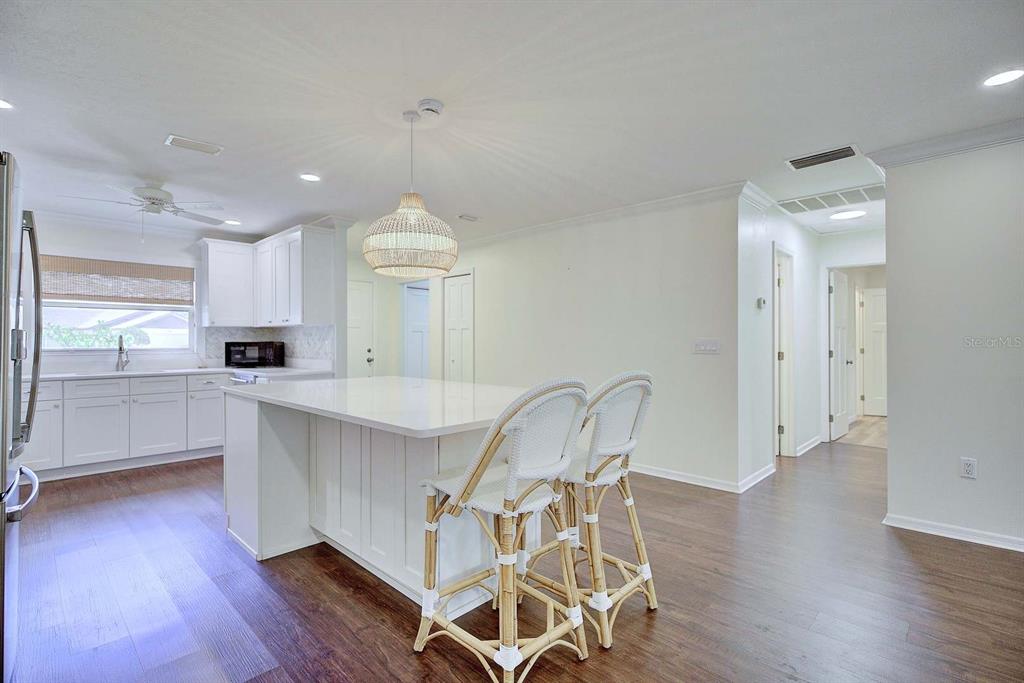 A kitchen features white cabinets, a central island with two stools, and dark wood flooring — 3855 RODEO DRIVE, SEBRING, FL