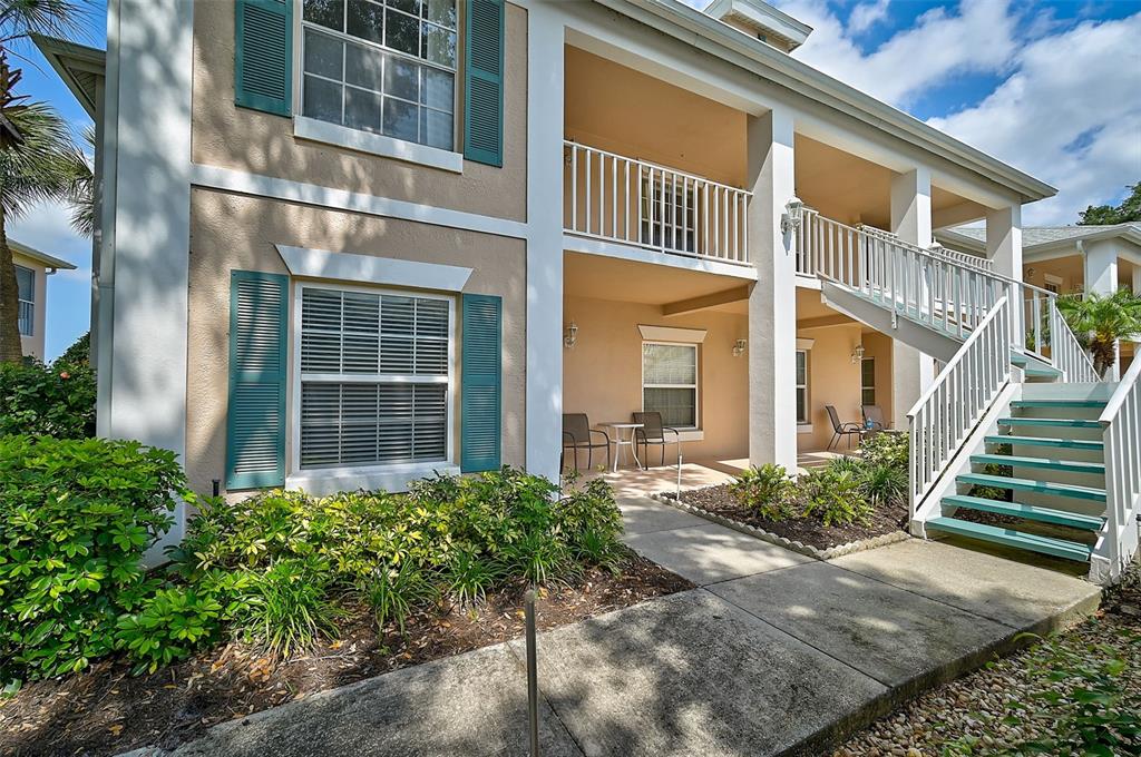A two-story apartment building exterior features a concrete staircase, balconies, and green shutters — 4215 CADDIE DRIVE E UNIT 101, BRADENTON, FL